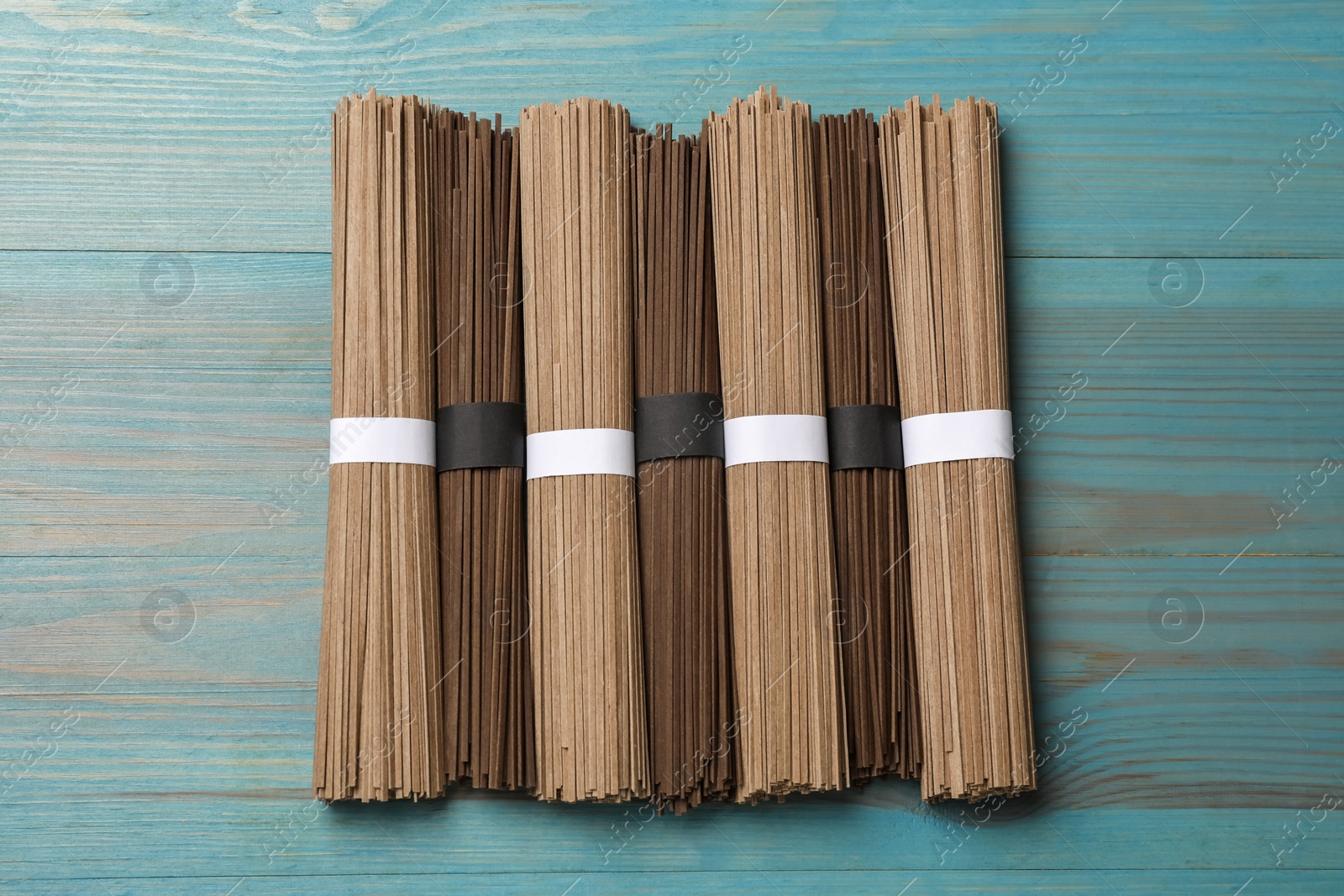 Photo of Uncooked buckwheat noodles (soba) on light blue wooden table, flat lay