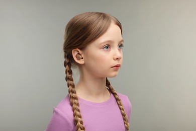 Photo of Little girl with hearing aid on grey background