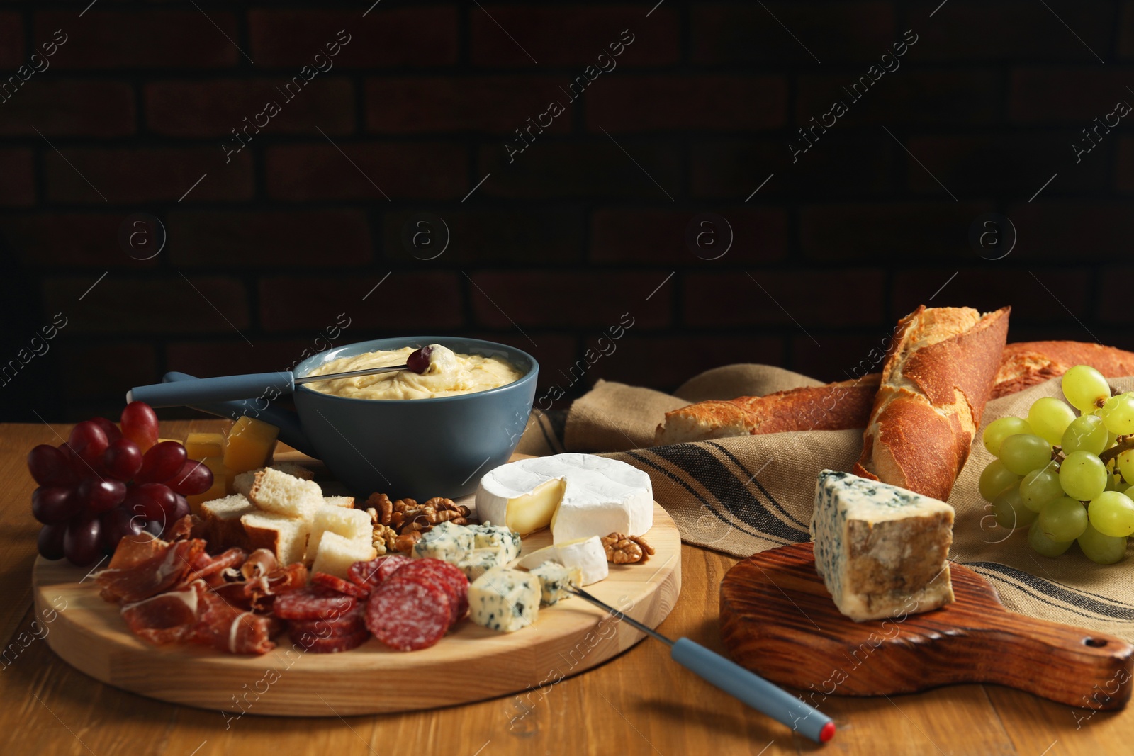 Photo of Fondue pot with tasty melted cheese, forks and different snacks on wooden table