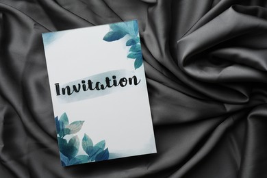 Photo of Beautiful card with word Invitation on black fabric, top view. Space for text