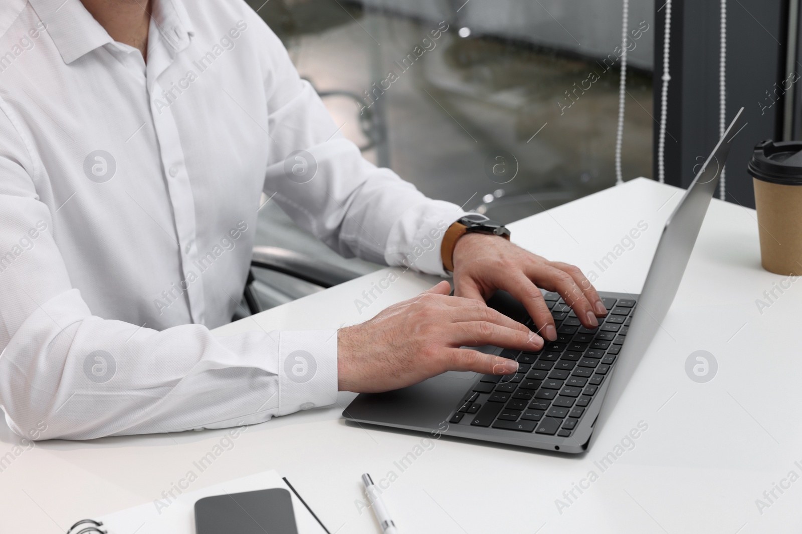 Photo of Man working on laptop at white desk in office, closeup