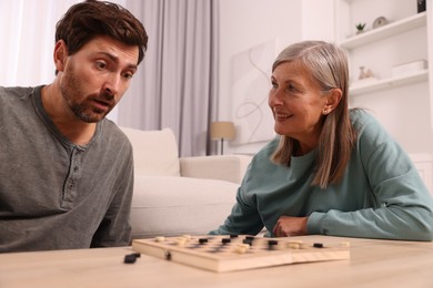 Family playing checkers at wooden table in room