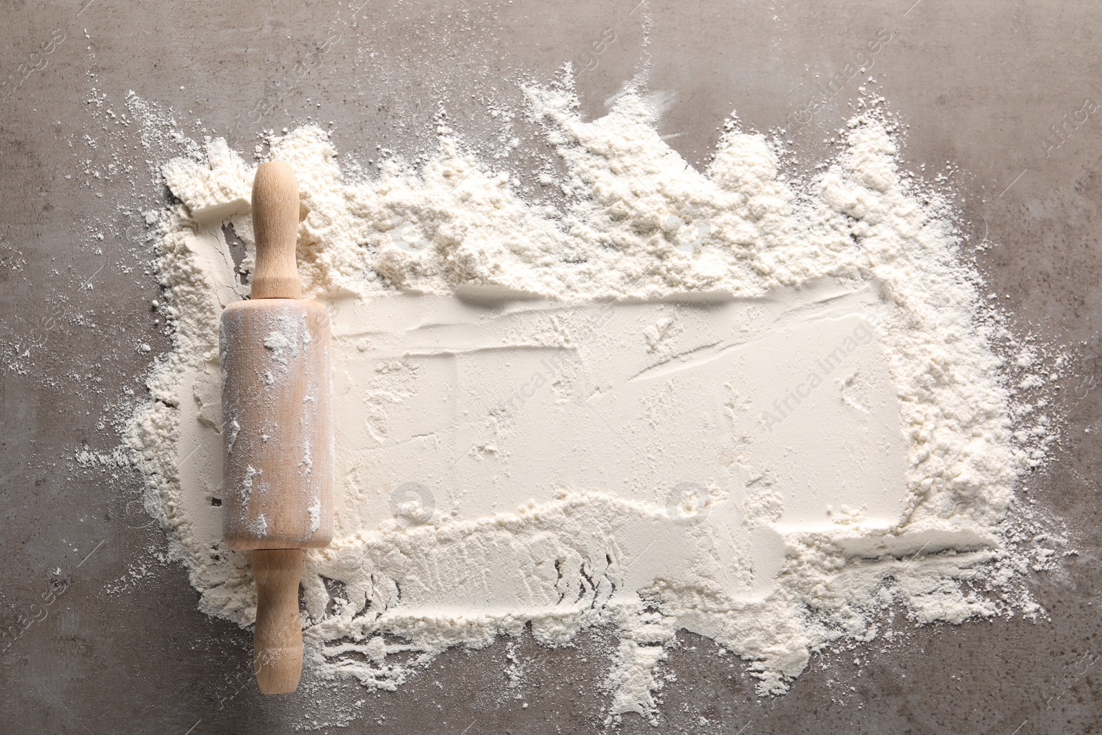 Photo of Scattered flour and rolling pin on grey textured table, top view