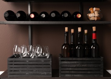 Photo of Bottles of wine, corks and glasses on rack near brown wall