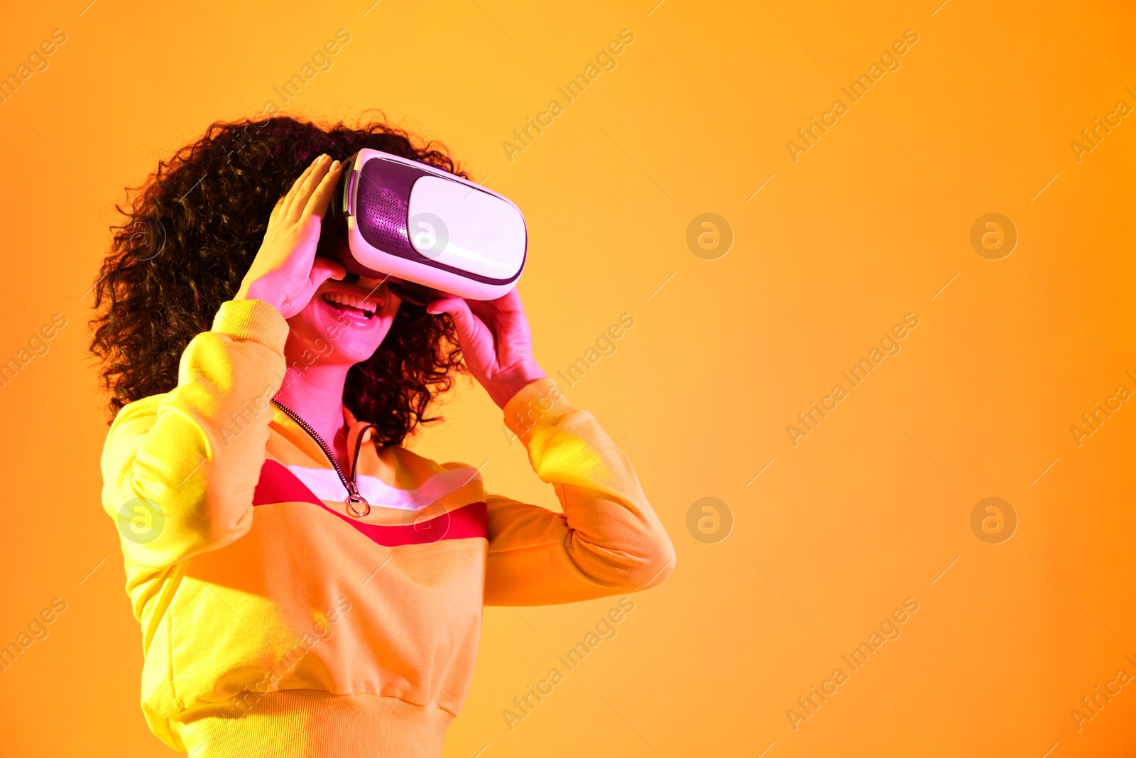 Photo of Beautiful young woman with virtual reality headset on color background in neon lights. Space for text