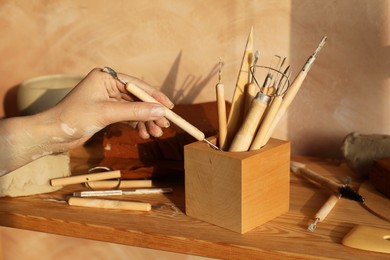 Photo of Woman taking clay crafting tool from wooden holder in workshop, closeup