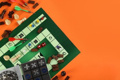 Photo of Different types of board games and its' components on orange background, flat lay. Space for text