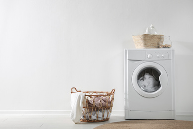 Modern washing machine and laundry baskets near white wall indoors, space for text. Bathroom interior