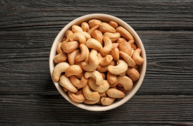 Photo of Bowl with cashew nuts on wooden table, top view