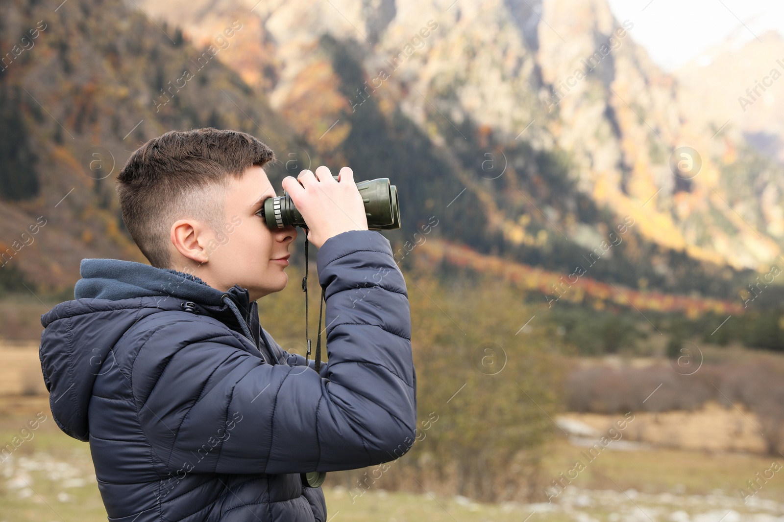Photo of Boy looking through binoculars in beautiful mountains. Space for text