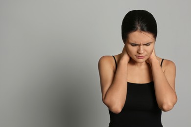 Photo of Young woman suffering from neck pain on grey background, space for text