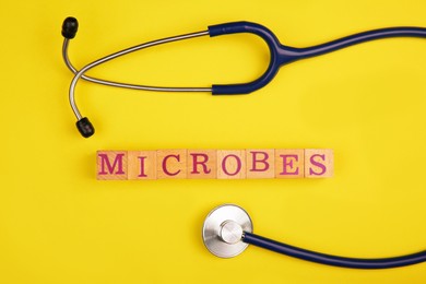 Photo of Word Microbes made with wooden cubes and stethoscope on yellow background, top view