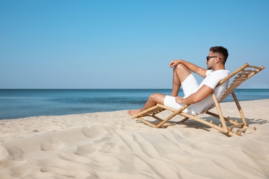 Photo of Young man relaxing in deck chair on sandy beach