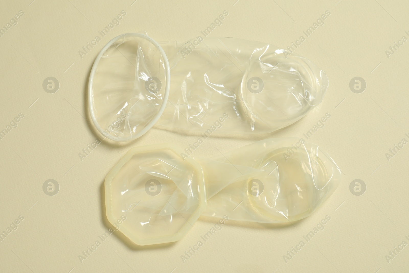 Photo of Unrolled female condoms on beige background, flat lay. Safe sex