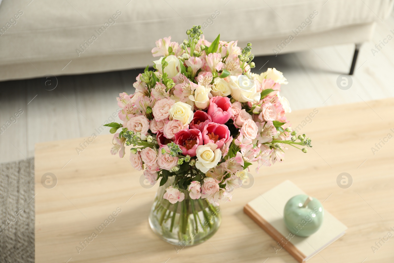 Photo of Beautiful bouquet of fresh flowers in vase and books on wooden table indoors