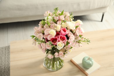 Beautiful bouquet of fresh flowers in vase and books on wooden table indoors