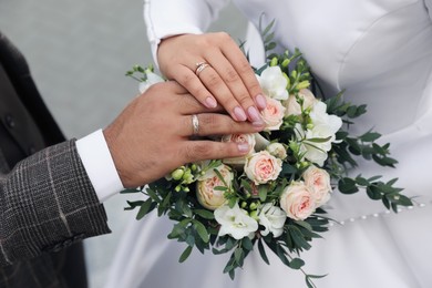 Photo of Bride and groom wearing beautiful engagement rings with bouquet outdoors, closeup