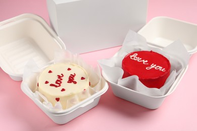 Photo of Tasty bento cakes in takeaway packagings on pink table