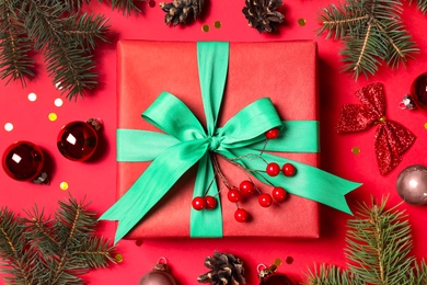 Gift box and fir branches with Christmas decoration on red background, flat lay