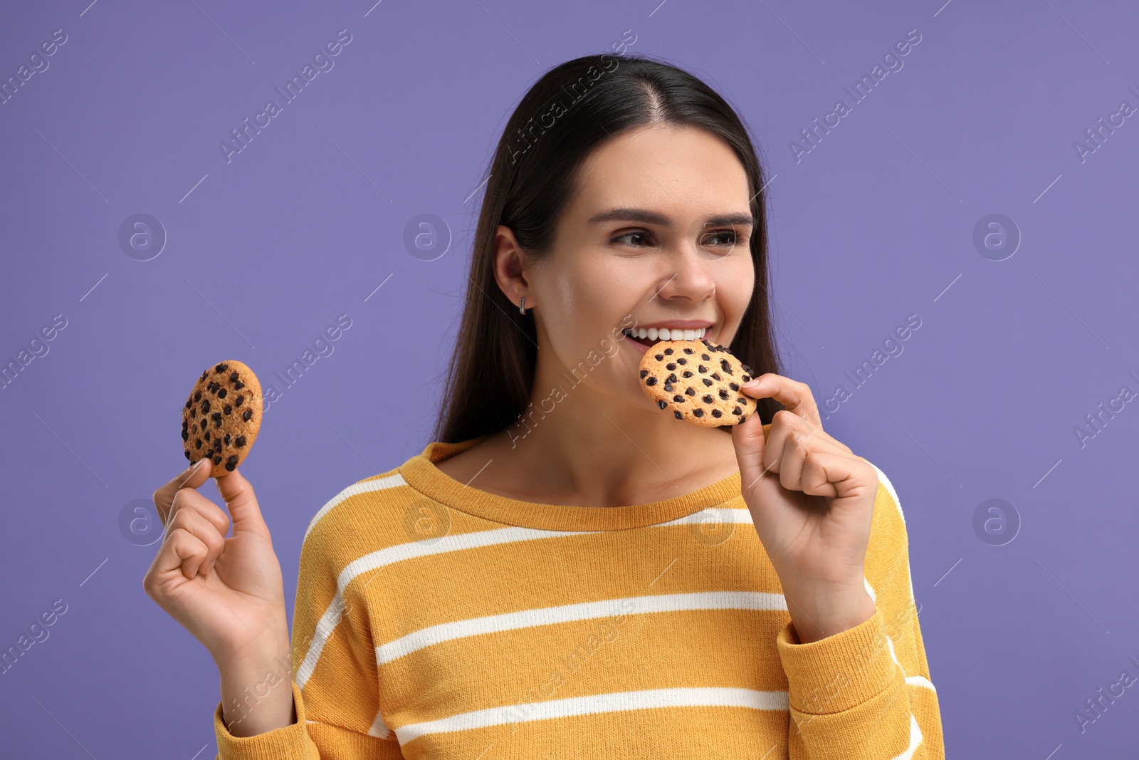 Photo of Young woman with chocolate chip cookies on purple background