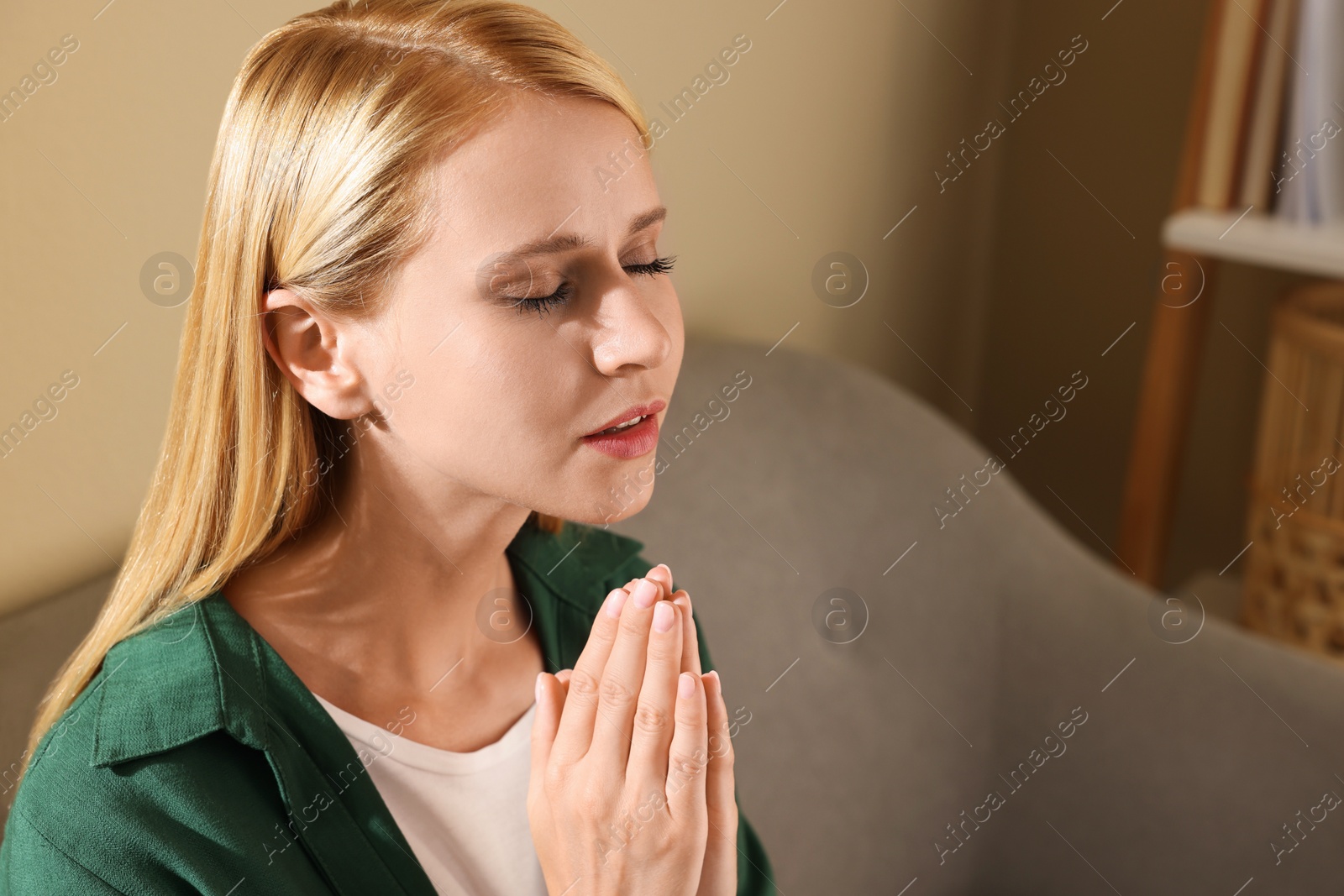 Photo of Religious young woman with clasped hands praying indoors. Space for text