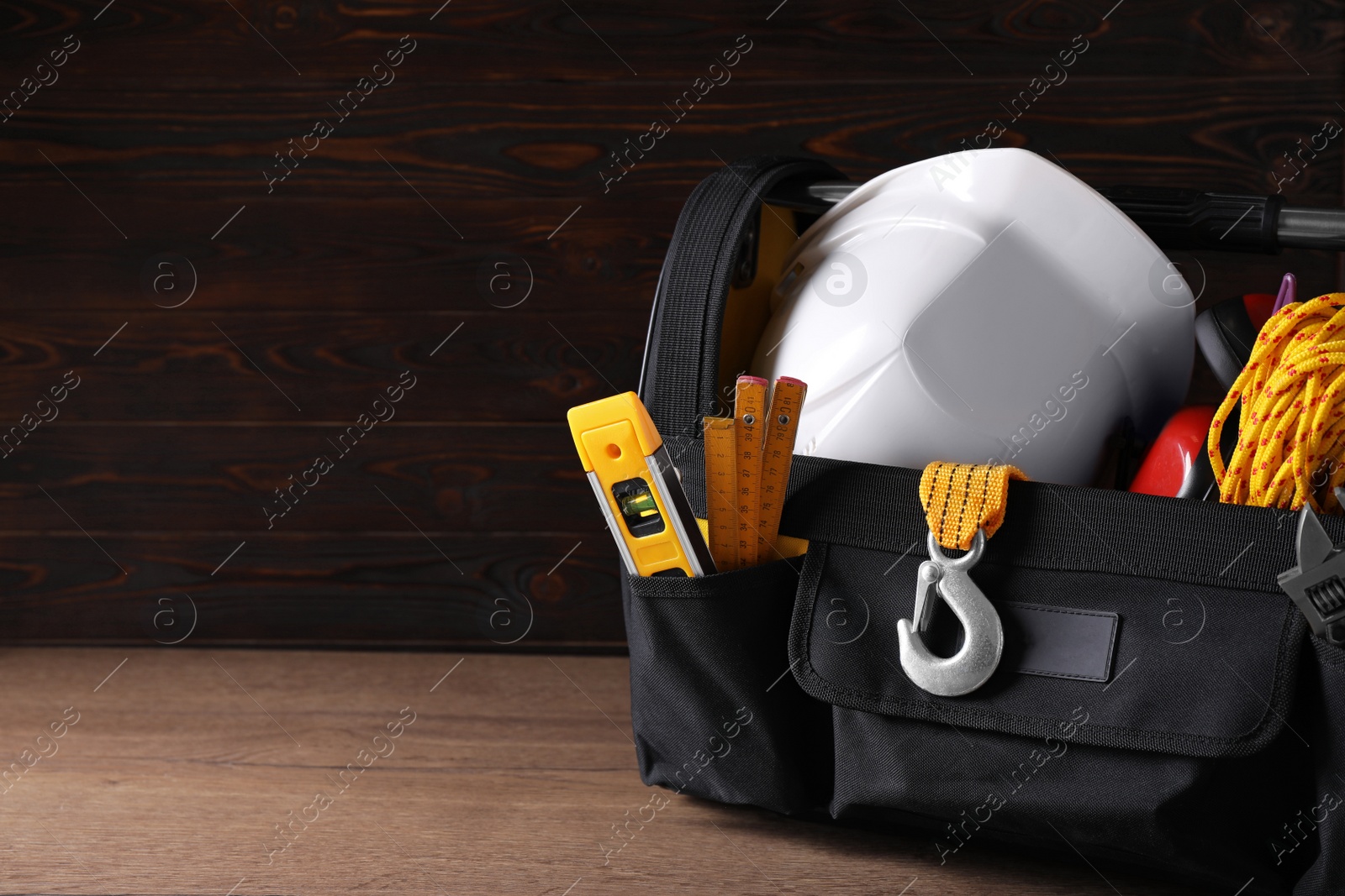 Photo of Black bag with construction tools on wooden table. Space for text