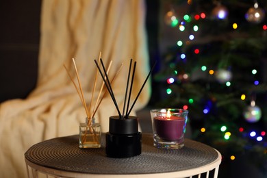 Photo of Aromatic reed air fresheners and candle on side table in cozy room