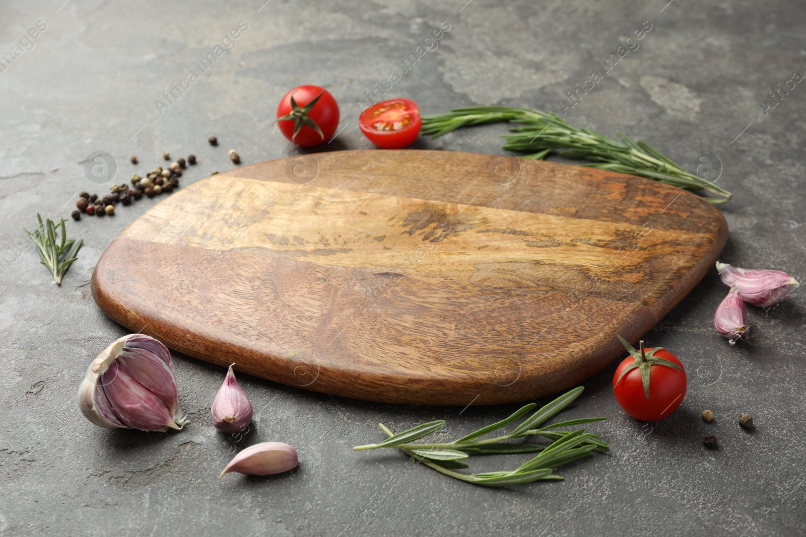 Photo of Cutting board, rosemary, garlic, pepper and tomatoes on black table. Space for text