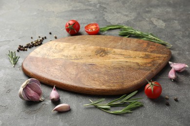 Photo of Cutting board, rosemary, garlic, pepper and tomatoes on black table. Space for text