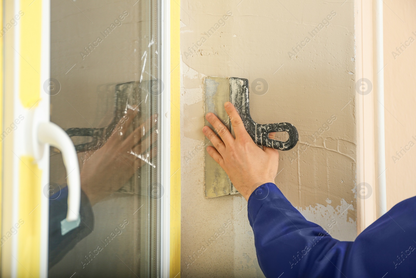 Photo of Professional worker plastering window area with putty knife indoors, closeup. Interior repair