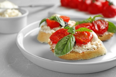 Photo of Plate of delicious tomato bruschettas on light grey marble table, closeup