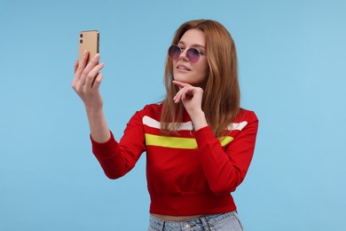 Photo of Beautiful woman in sunglasses taking selfie on light blue background