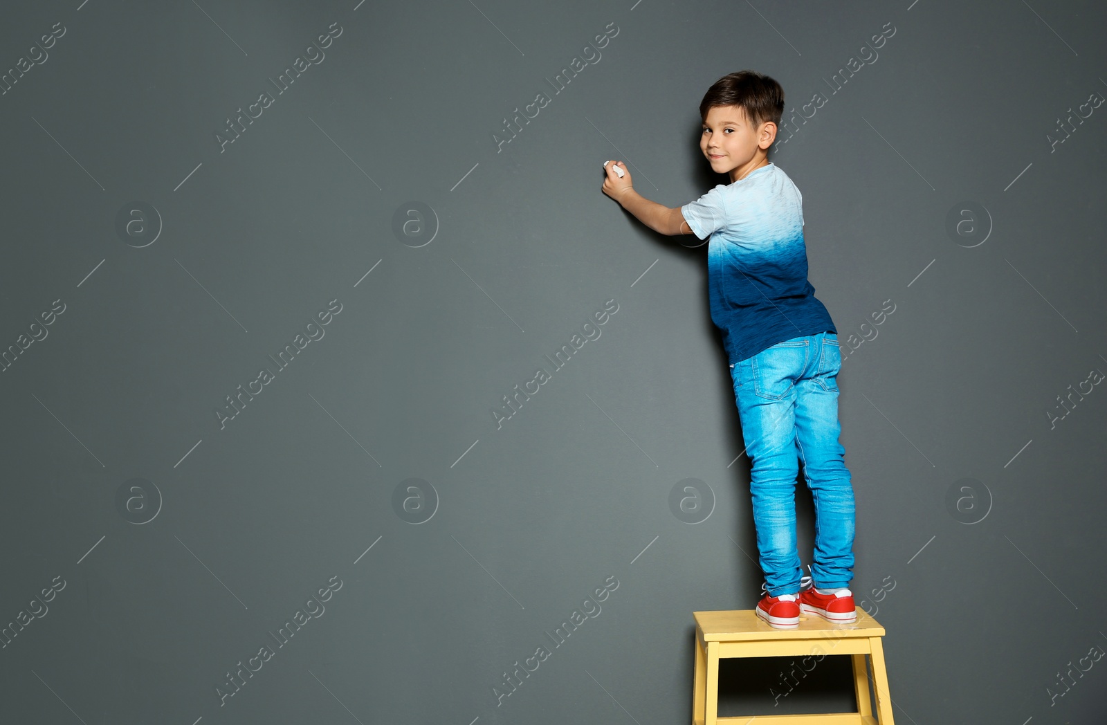 Photo of Little child drawing with chalk on gray wall. Space for text