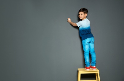 Little child drawing with chalk on gray wall. Space for text