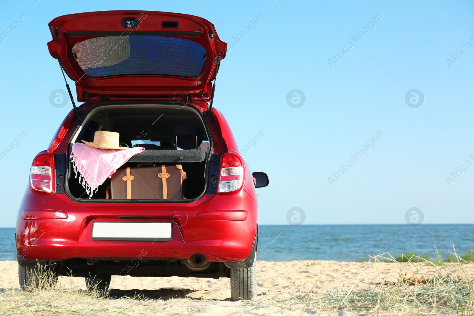 Photo of Retro suitcase and beach accessories in car trunk on sand near sea. Space for text