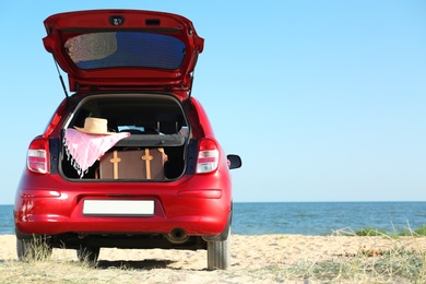 Photo of Retro suitcase and beach accessories in car trunk on sand near sea. Space for text