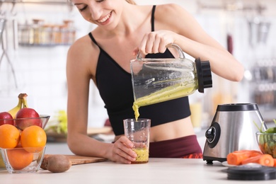 Photo of Young woman pouring tasty healthy smoothie into glass at table in kitchen