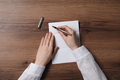 Woman writing letter at wooden table, top view