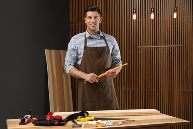 Photo of Handsome carpenter with folding rule near wooden wall
