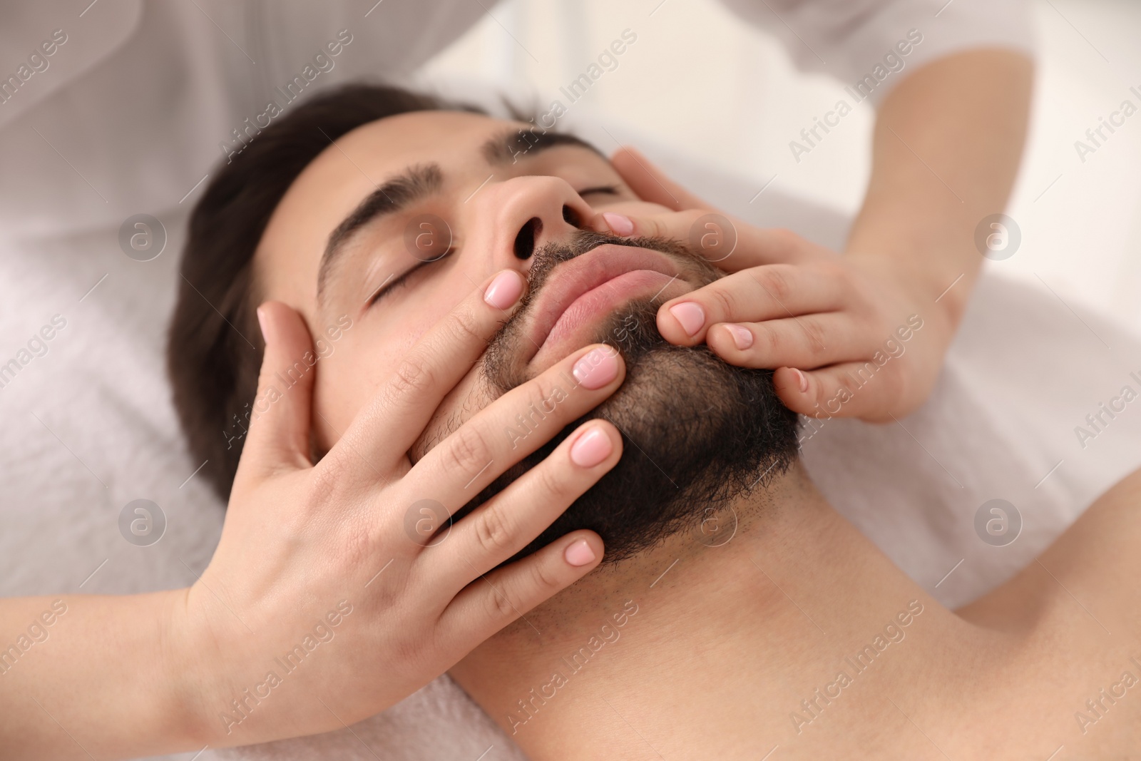 Photo of Young man receiving facial massage in beauty salon, closeup