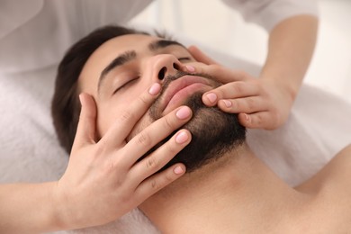 Young man receiving facial massage in beauty salon, closeup