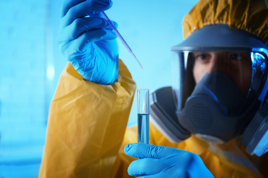 Scientist in chemical protective suit dripping reagent  into test tube at laboratory, focus on hands. Virus research