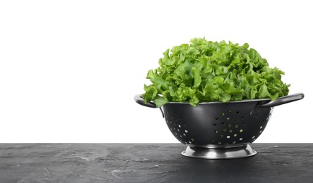 Photo of Metal colander with fresh lettuce on black textured table against white background, space for text