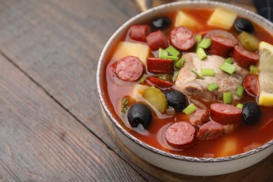 Meat solyanka soup with thin dry smoked sausages in bowl on wooden table, closeup. Space for text