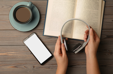 Photo of Woman holding headphones over wooden table with book, top view