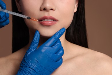 Photo of Woman getting lip injection on brown background, closeup