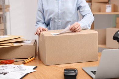 Photo of Parcel packing. Post office worker sticking barcode on box at wooden table indoors, closeup