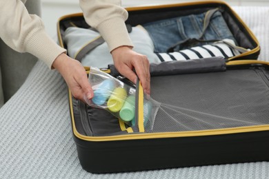 Photo of Woman with plastic bag of cosmetic travel kit packing suitcase, closeup. Bath accessories