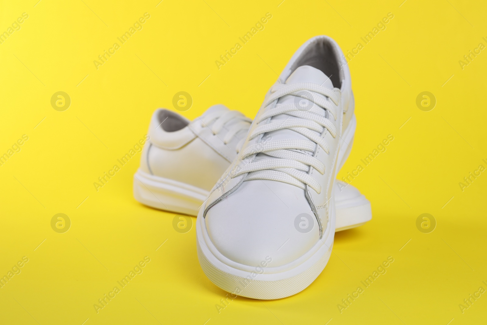 Photo of Pair of stylish white sneakers on yellow background