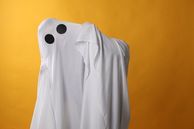 Creepy ghost. Person covered with white sheet on yellow background, space for text